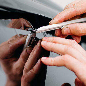 Technician cutting tint film on a car windows with a cutter